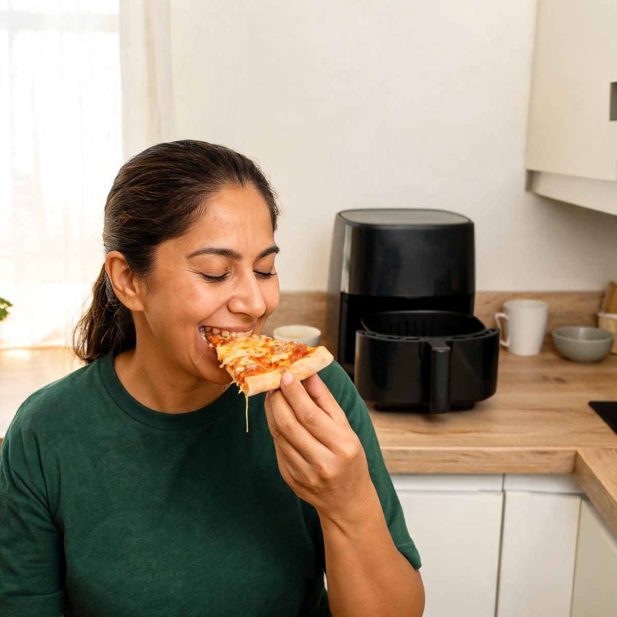 Mulher sorrindo ao morder uma fatia de pizza recém-saída da air fryer